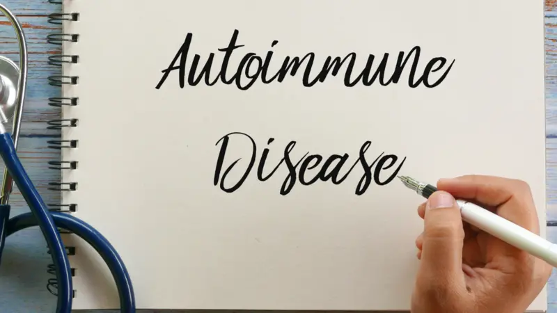 Top view of stethoscope, pen and hand writing ' Autoimmune Disease ' on notebook on wooden background