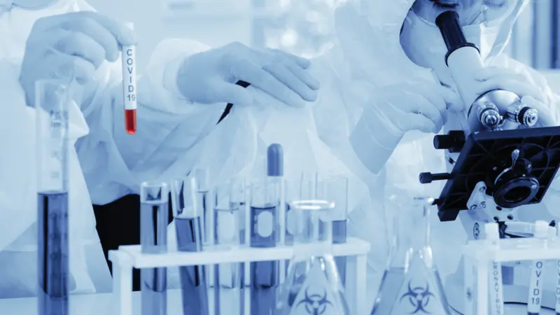 scientist analyzing covid 19 sample with microscope and holding coronavirus covid 19 blood sample tube scientist analyzing covid 19 sample with microscope and holding coronavirus covid 19 blood sample tube