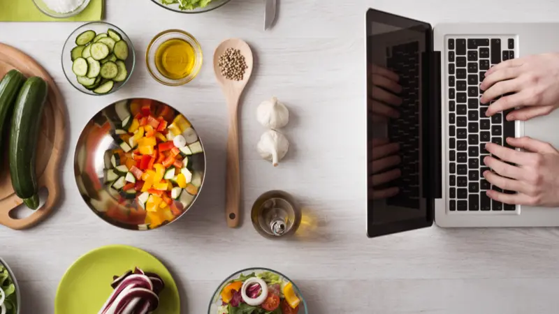 laptop with food ingredients and fresh vegetables on the left, top view