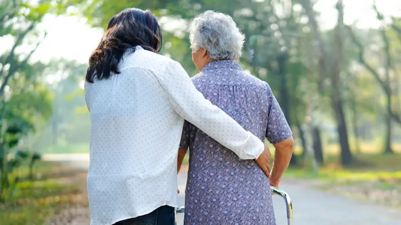 Helping senior woman use walker while walking at park 