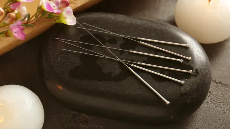 Acupuncture needles with stone and candles on textured background