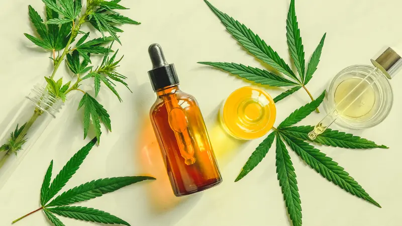 Various glass bottles with CBD oil, THC tincture and hemp leaves on a marble background