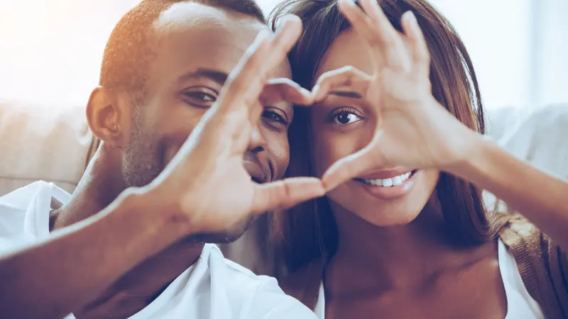 couple sitting close to each other and looking through a heart shape made with their fingers