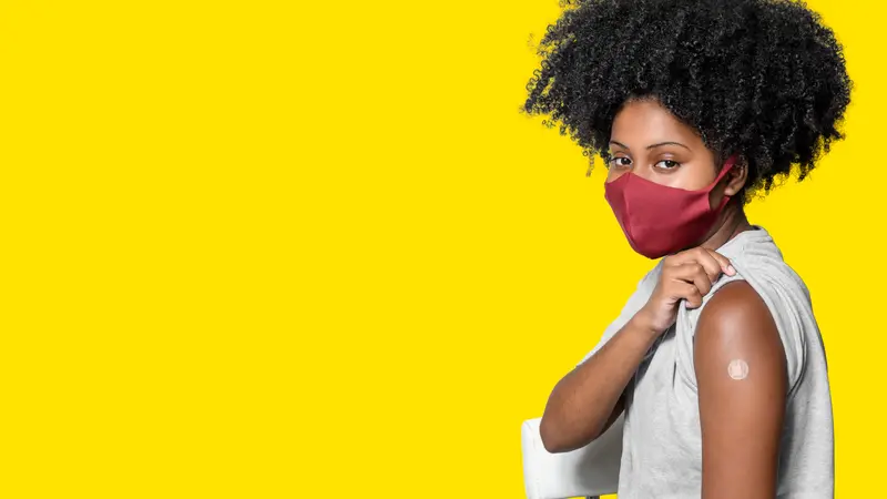 woman wearing protective mask shows the vaccine bandage, isolated on yellow background