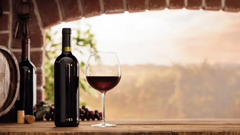 wineglass and bottles next to the window and panoramic view of vineyards at sunset