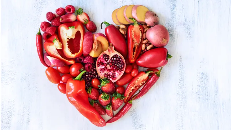 Collection of fresh red vegetables and fruits arranged in a heart shape on white rustic background strawberry raspberry pomegranate peppers capsicum chilli potato beans