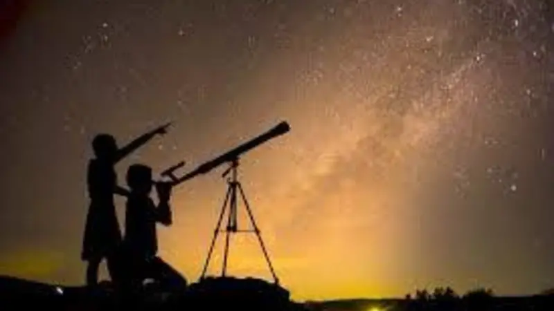 Silhouette of a parent and child looking into a telescope and pointing at the night sky. 