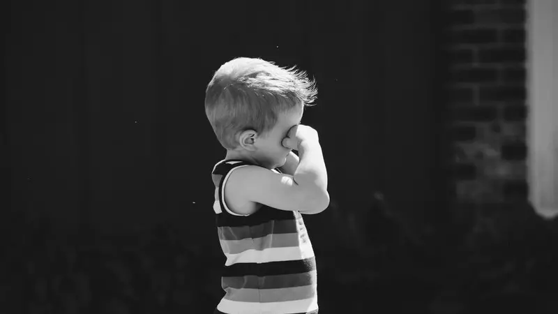 black and white photo of a small child with striped tank top rubbing his eyes