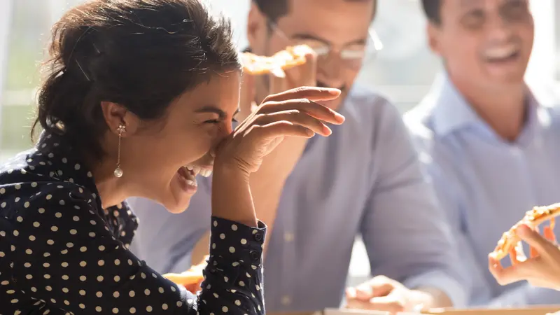 Laughing indian businesswoman in friends company eating pizza enjoy lunch together with colleagues