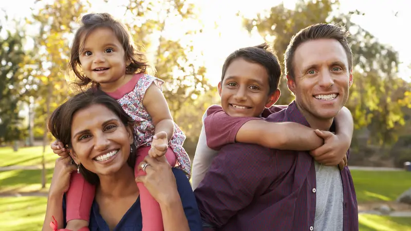 Mixed race parents carry their kids piggyback in a park