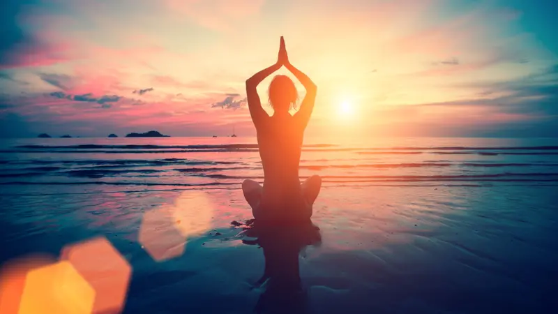 Silhouette young woman practicing yoga on the beach at sunset. Meditation.