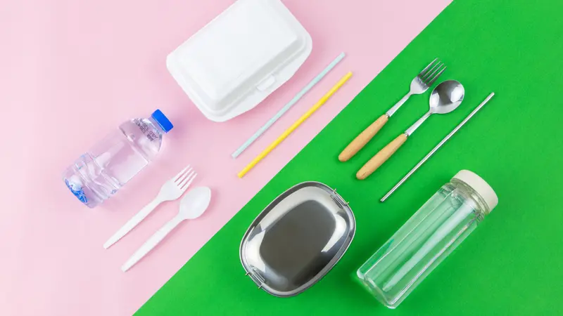 Flat lay photo comparison between disposable foam container, plastic cutlery, plastic straw, plastic bottle and reusable lunch box, spoon, fork straw and water bottle on two colours, pink and green.