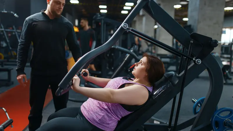 Overweight woman with trainer doing exercise on weight machine