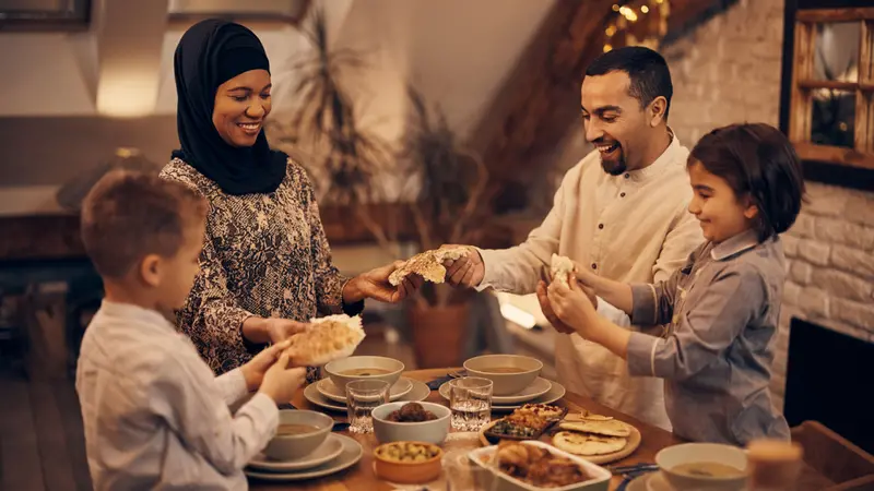 Happy Muslim parents and their kids sharing pita bread while eating dinner