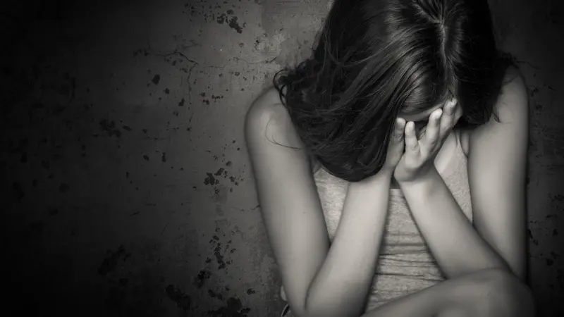 Black and white grunge image of a beautiful teenage girl sitting on the floor crying