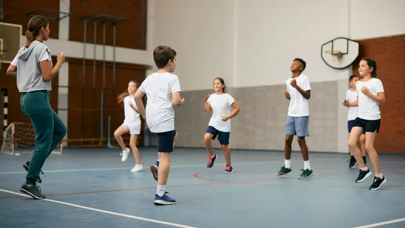 Group of elementary students having PE class with their sports teacher at school gym