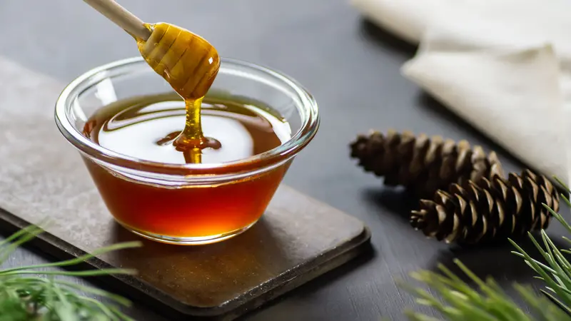 Bowl with honey stick and pine cones on rustic table