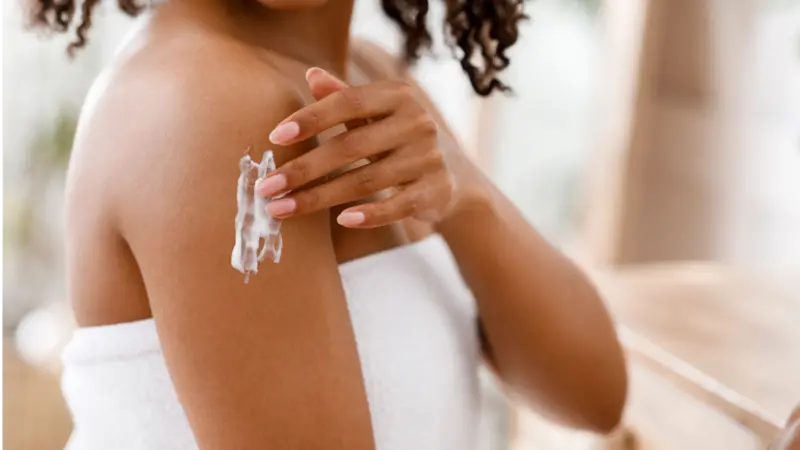 Black woman applying moisturizing lotion on body after shower