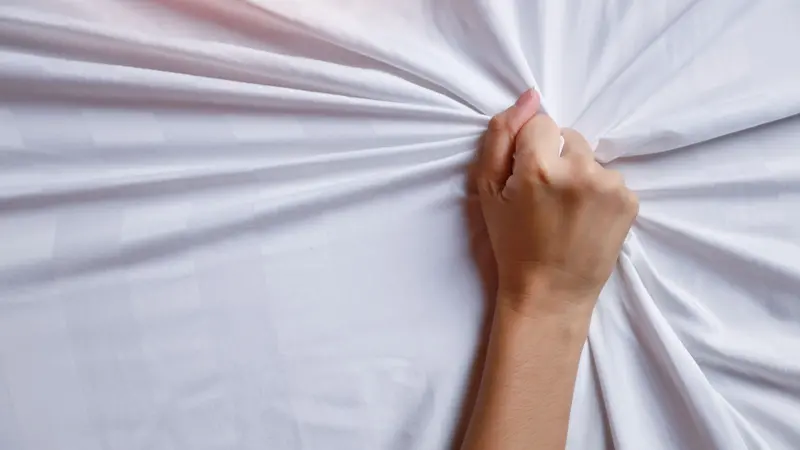 Close up young woman hands pulling white sheets in ecstasy