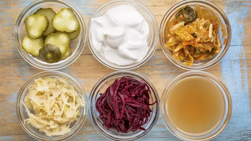 a set of fermented food great for gut health - top view of glass bowls against grunge wood: cucumber pickles, coconut milk yogurt, kimchi, sauerkraut, red beets, apple cider vinegar