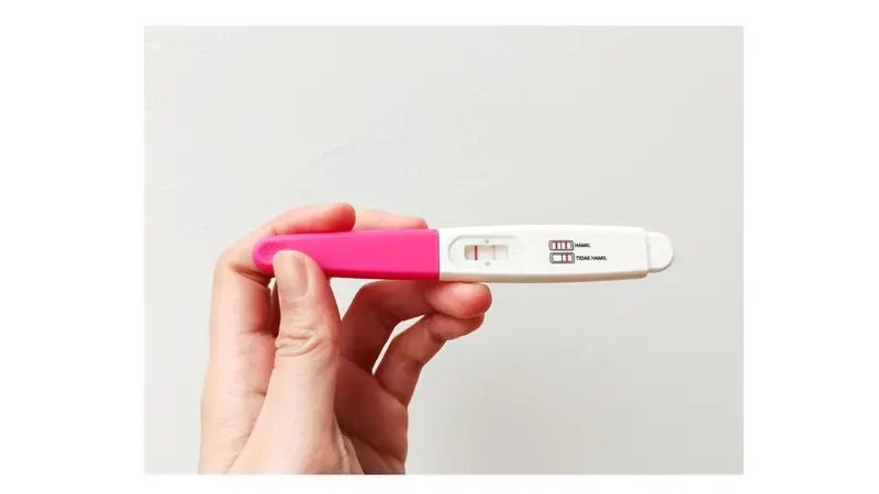 A woman's hand holding a positive pregnancy test on a white background