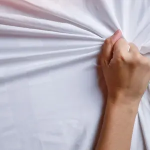 Close up young woman hands pulling white sheets in ecstasy