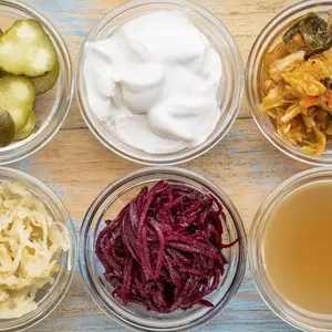 a set of fermented food great for gut health - top view of glass bowls against grunge wood: cucumber pickles, coconut milk yogurt, kimchi, sauerkraut, red beets, apple cider vinegar