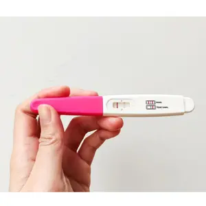 A woman's hand holding a positive pregnancy test on a white background