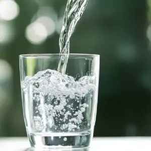 Pouring Water into a Glass Against a Green Blurred Background