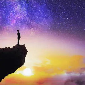 Man standing on edge of cliff with colorful sky Man standing on edge of cliff with colorful sky