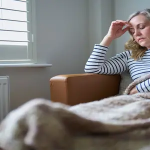 woman sitting on the couch rubbing her head in pain/fatigue, suffering from long COVID woman sitting on the couch rubbing her head in pain/fatigue, suffering from long COVID